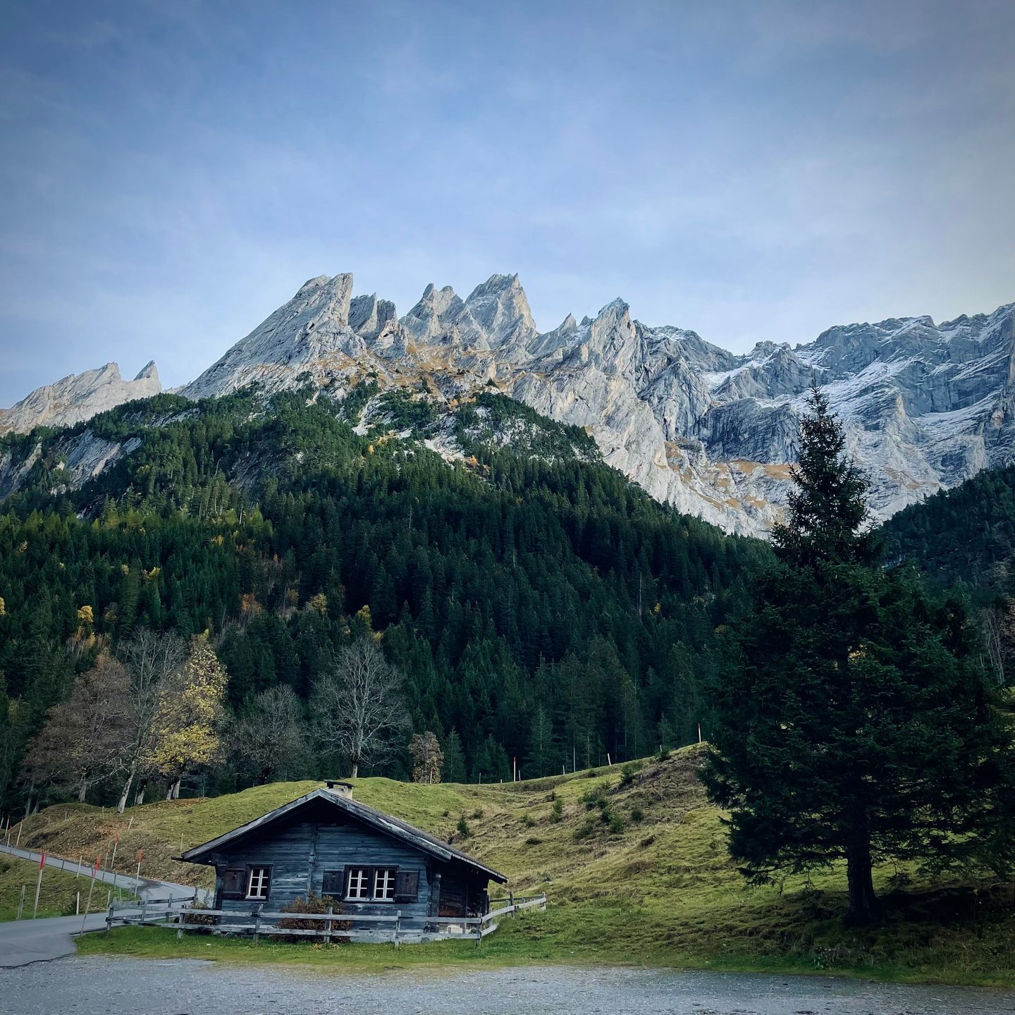 A timber mountain hut in a green valley below jagged limestone peaks