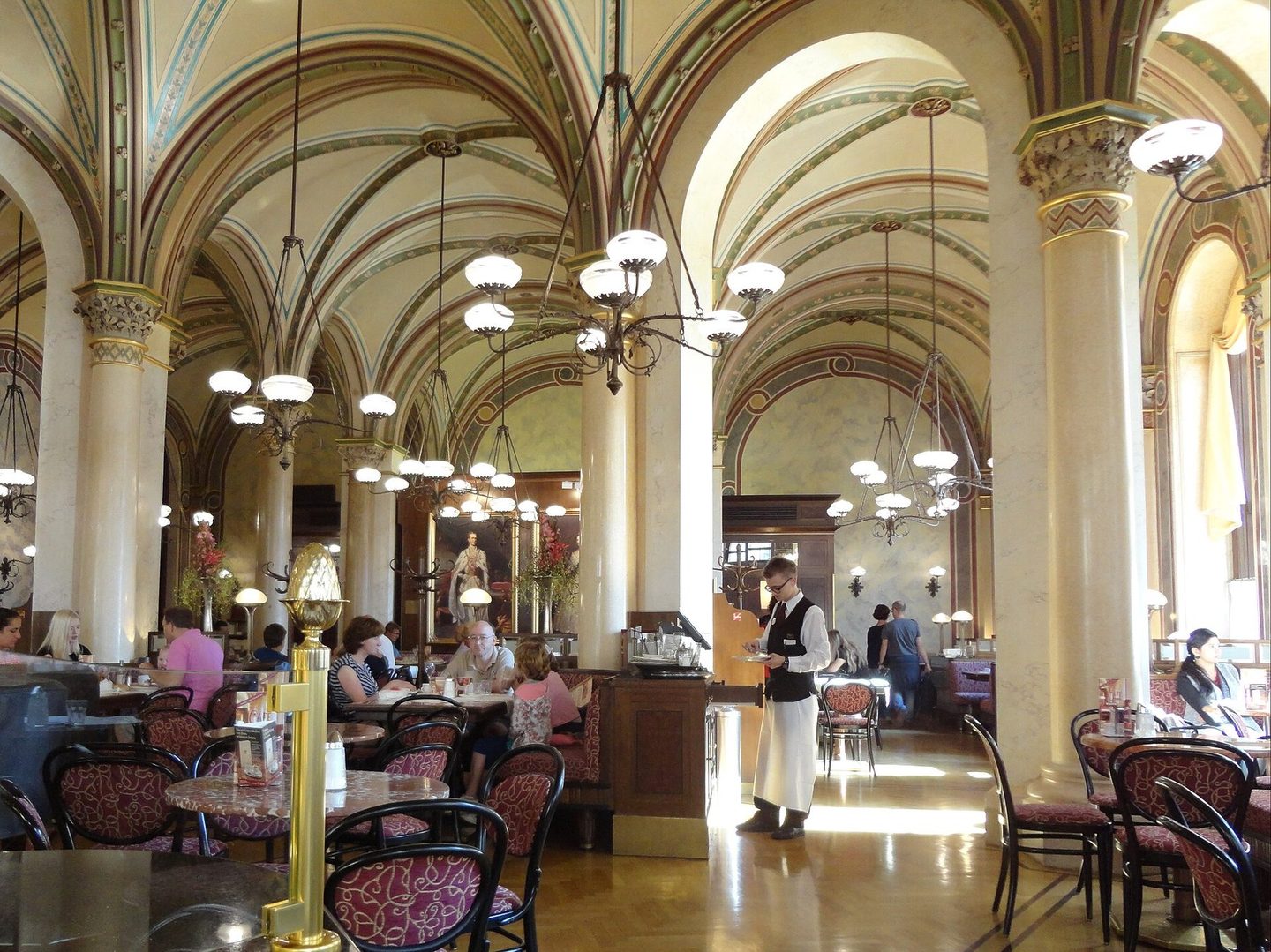 The vaulted interior of a Viennese coffee house, with marble tables and a waiter