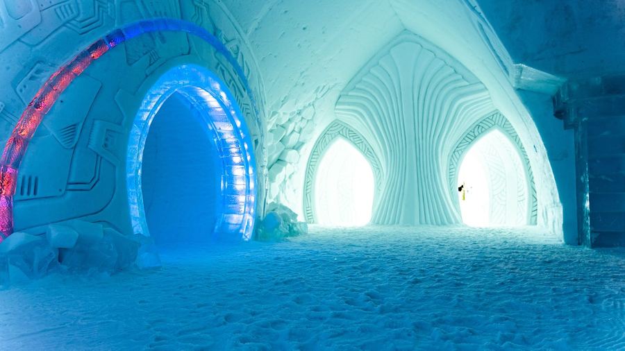 A hall carved from snow and ice, lit blue and pink, with arched doorways and a snow-packed floor