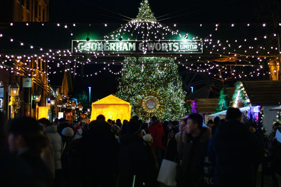 A dense evening crowd under strings of lights beneath a Gooderham and Worts sign, with a lit Christmas tree behind