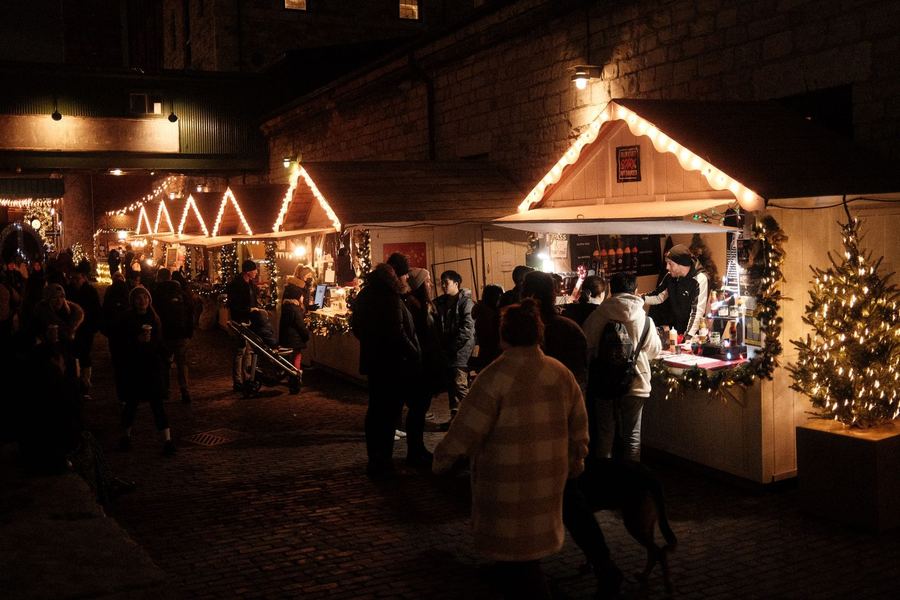 A crowded Christmas market lane under strings of festive lights