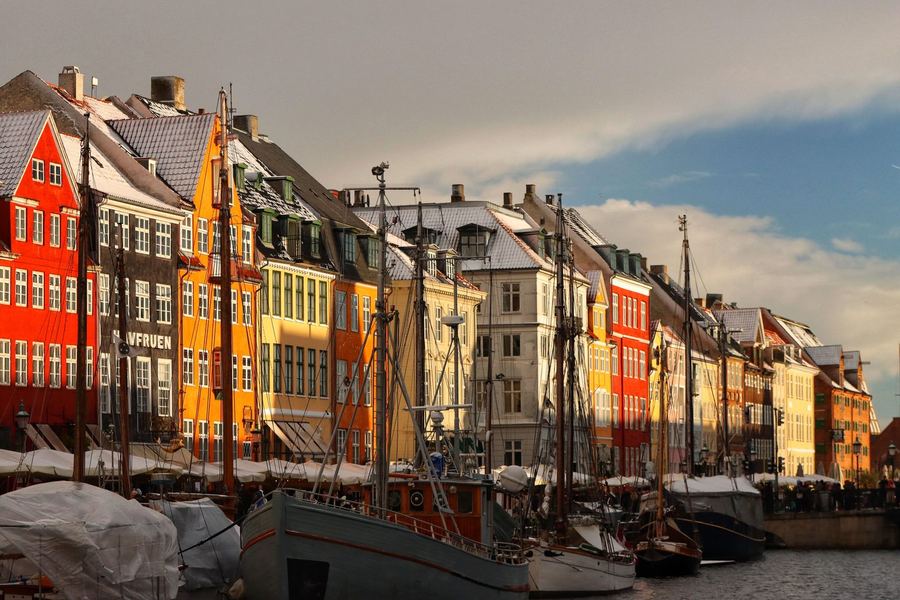 Snow on the roofs of the coloured houses along Nyhavn, with the masts of moored wooden boats in front of them