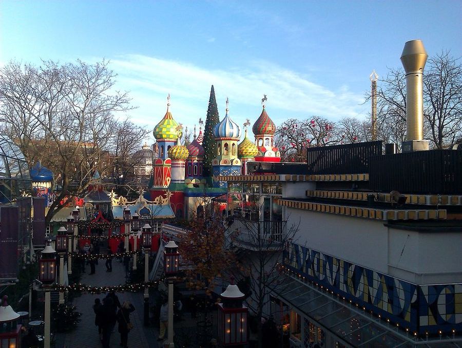 Painted onion-domed pavilions and a tall Christmas tree above a lantern-lined avenue at Tivoli, in daylight