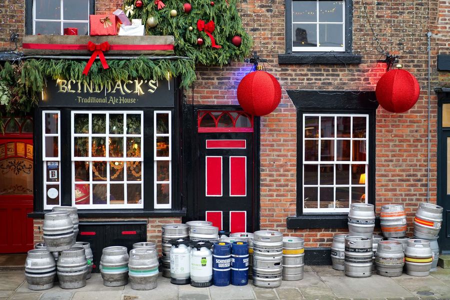 A brick pub front decorated with a Christmas tree, greenery and two large red baubles, with beer kegs stacked on the pavement