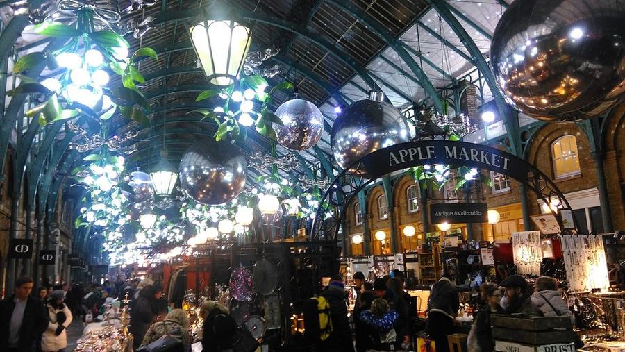 Giant silver baubles and lit greenery hanging from the iron and glass roof of Covent Garden's Apple Market, stalls below