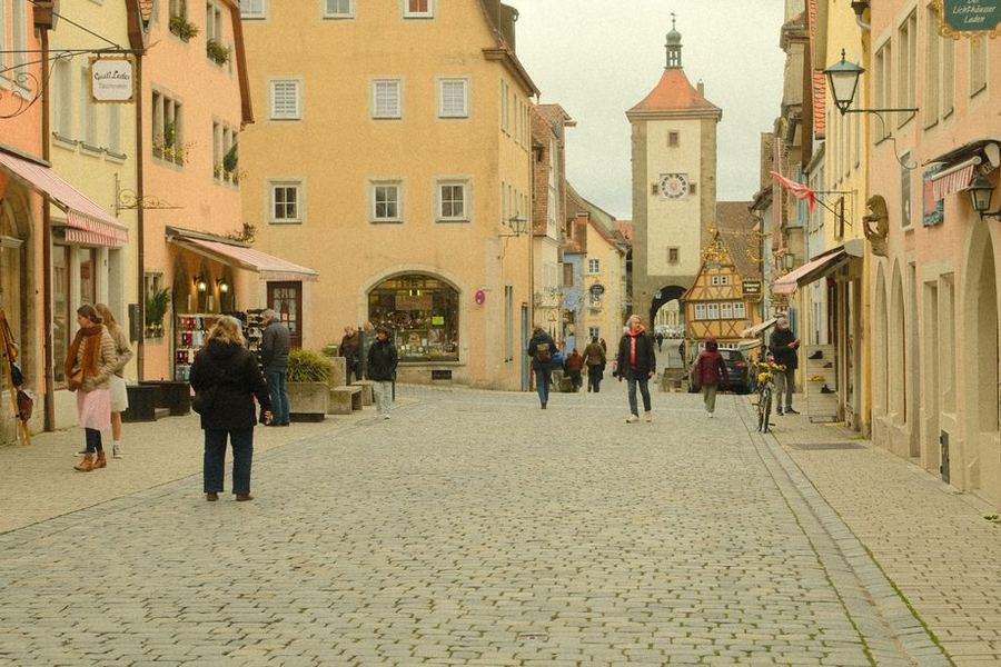 A wide cobbled street of pastel houses in Rothenburg leading to a tall clock tower and gateway, with a few shoppers