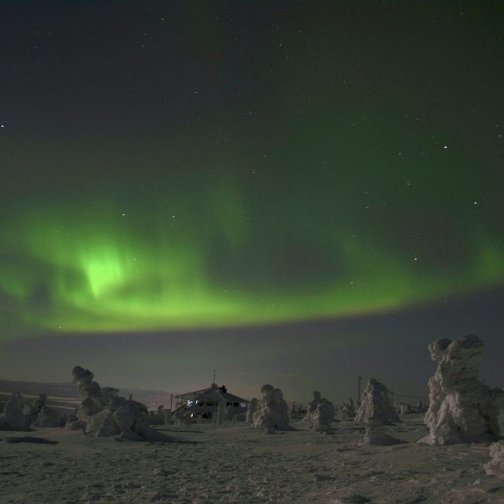 Green aurora over snow-covered fells and a lone cabin at night