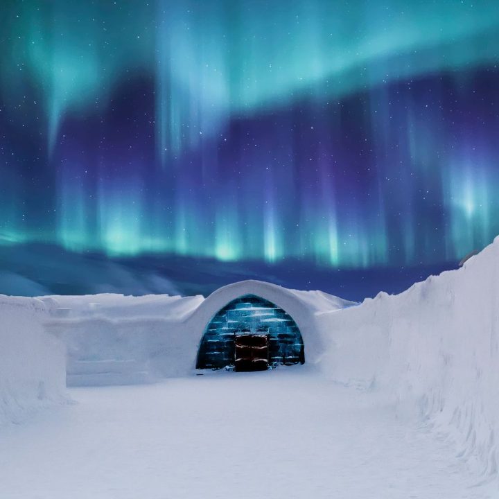 A snow igloo lit from inside beneath the northern lights