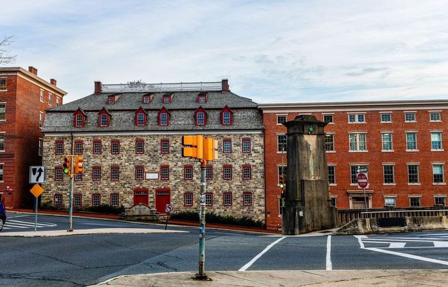 A large colonial-era stone building with red-framed windows and rows of dormers, beside a red brick block at a street corner